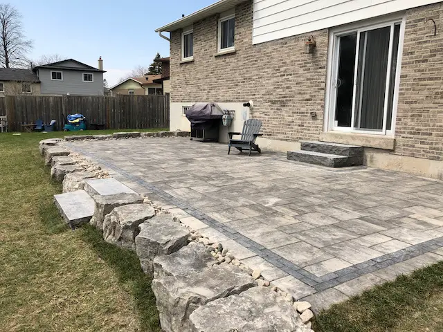 Large interlocking stone patio with natural stone retaining wall and large granite steps